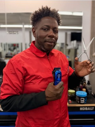 Dave in a red smock holding clippers and shears at the mirror