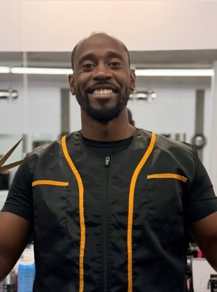 Bon(face) in a black and gold smock smiling at the mirror
